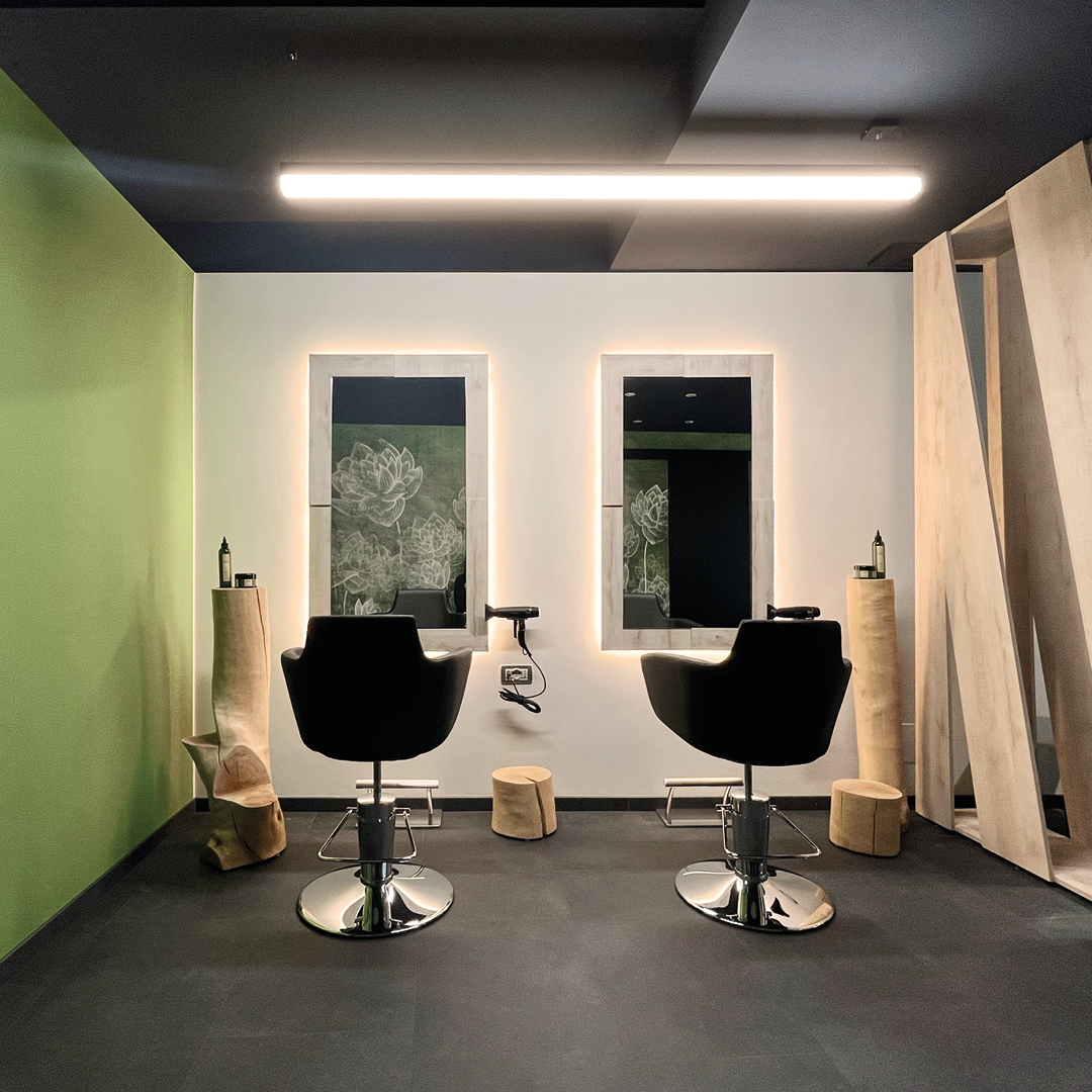 Immagine di due postazioni dell'area stilistica con poltrone nere, pareti verdi, specchi grandi e rettangolari e mobilio decorativo in legno 